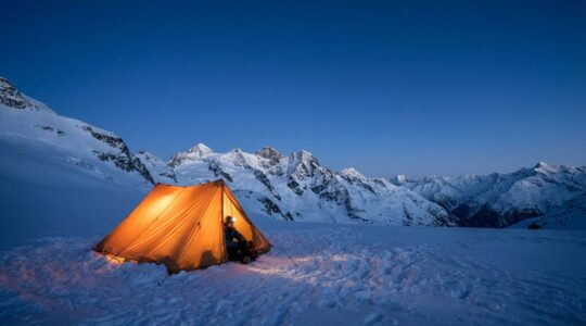 Bivouac hivernal dans la neige avec tente éclairée de l'intérieur sous un ciel étoilé